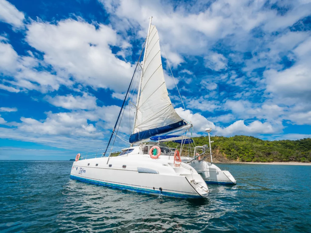 A white sailing catamaran anchored in the calm turquoise waters off Playa Flamingo with a lush green hillside and blue sky in the background, Guanacaste, Costa Rica