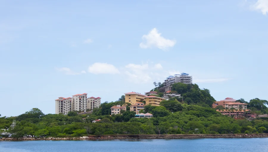 Lush tropical greenery and native trees covering the hillside of Playa Flamingo, with residential and resort buildings nestled among the canopy, viewed from the bay, Guanacaste, Costa Rica