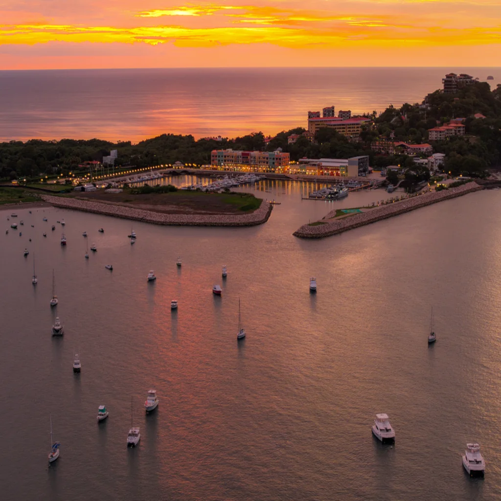 Aerial view of Marina Flamingo at sunset, with boats anchored in the bay and the marina lights reflecting on the calm water, Playa Flamingo, Costa Rica
